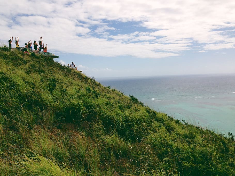 People Standing on a Green Mountain Peak Watching the Clear Blue Body of Water HD wallpaper