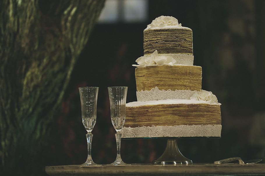 two clear wine glasses beside 3-layer towel cake, focus on foreground HD wallpaper