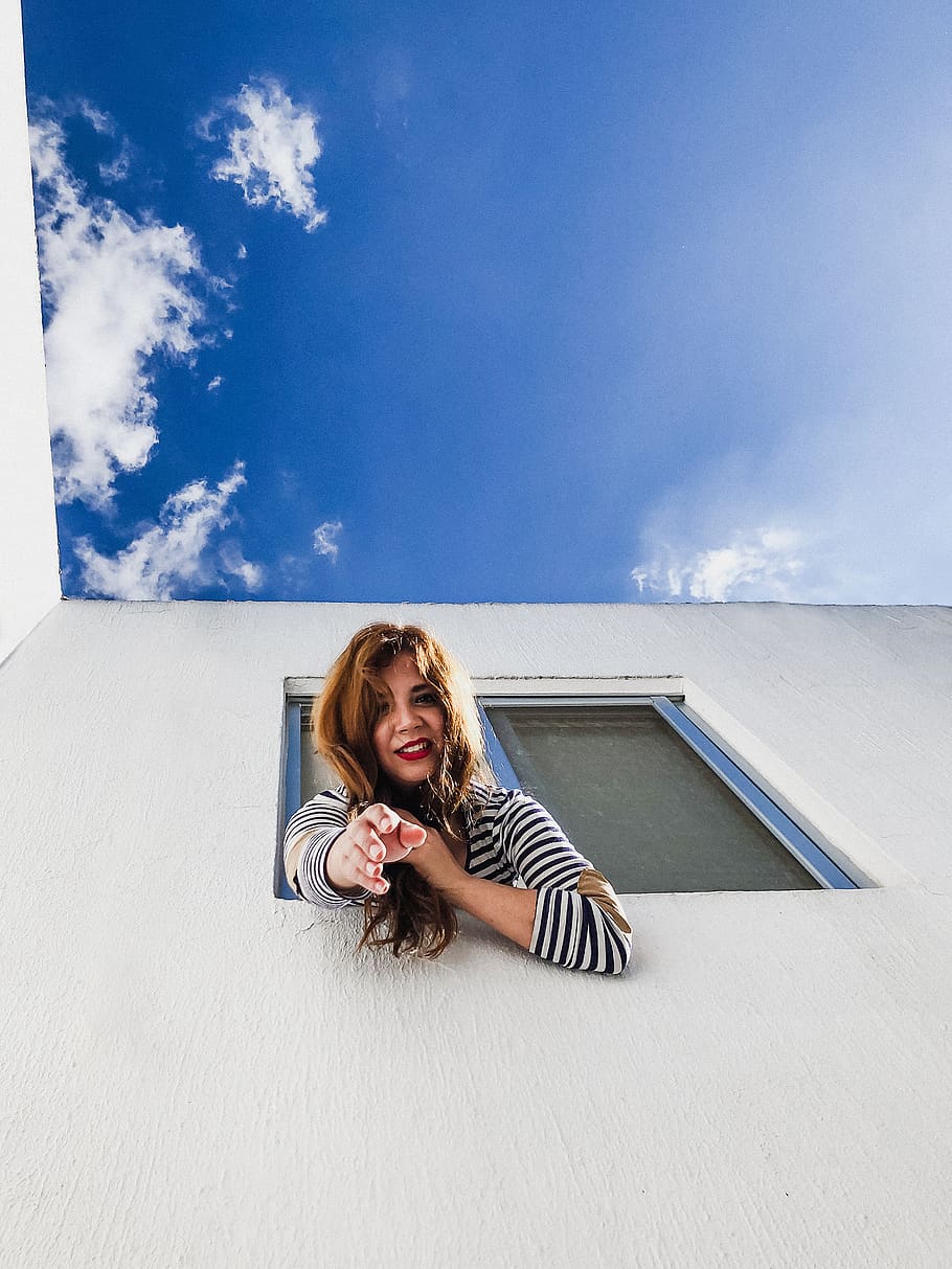 woman on window reaching her hands down under blue sky, person