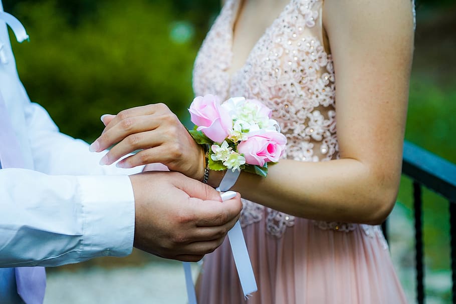 man putting pink and white floral decor to woman's hand, person