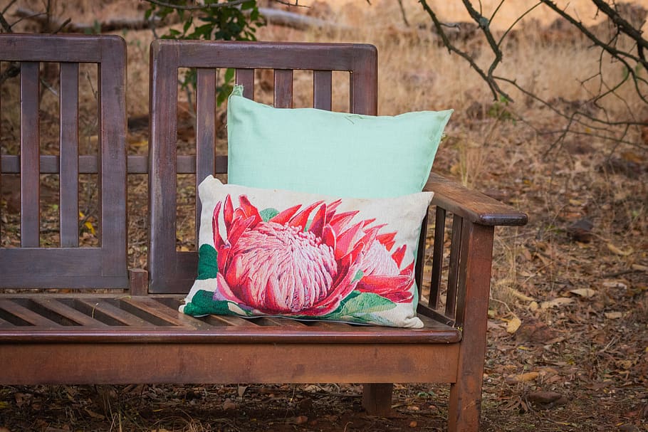 White Pillow With Lotus-printed on Brown Wooden Bench at the Park HD wallpaper
