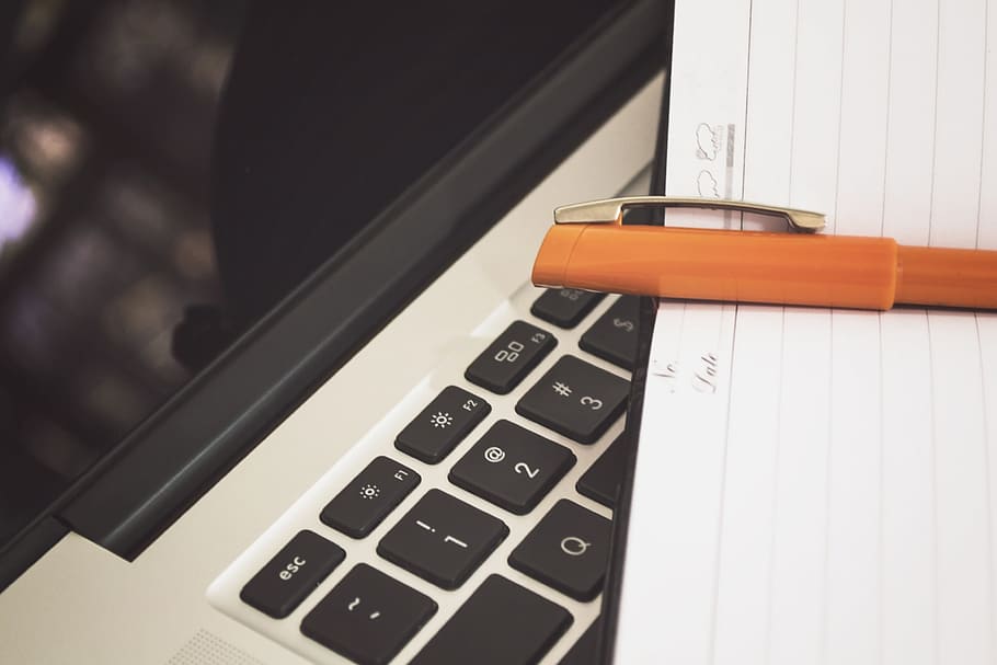 Note Taking Leather Notepad with an Orange Pen Placed on MacBook Keyboard HD wallpaper
