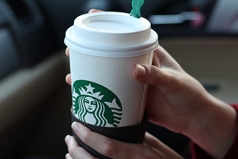 Tazza starbucks con dentro una cannuccia e una mano che la tiene ai  generativa