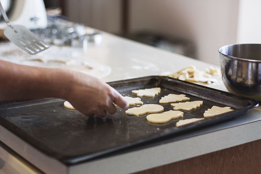 person lining assorted-shaped cookies on baking sheet inside kitchen HD wallpaper