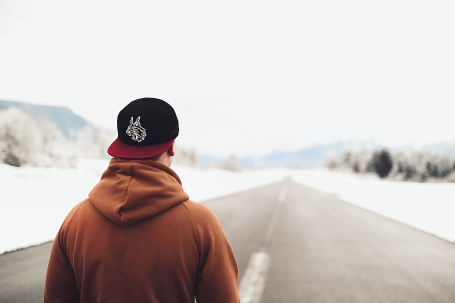 Person in Brown Hoodie and Fitted Cap Walking on Road, blurred background HD wallpaper