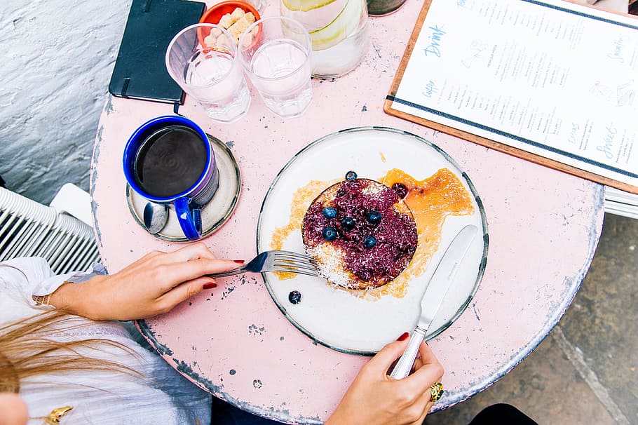 Woman Holding Spoon and Fork With Blackberries on Plate Beside Blue Ceramic Mug on White Wooden Table HD wallpaper