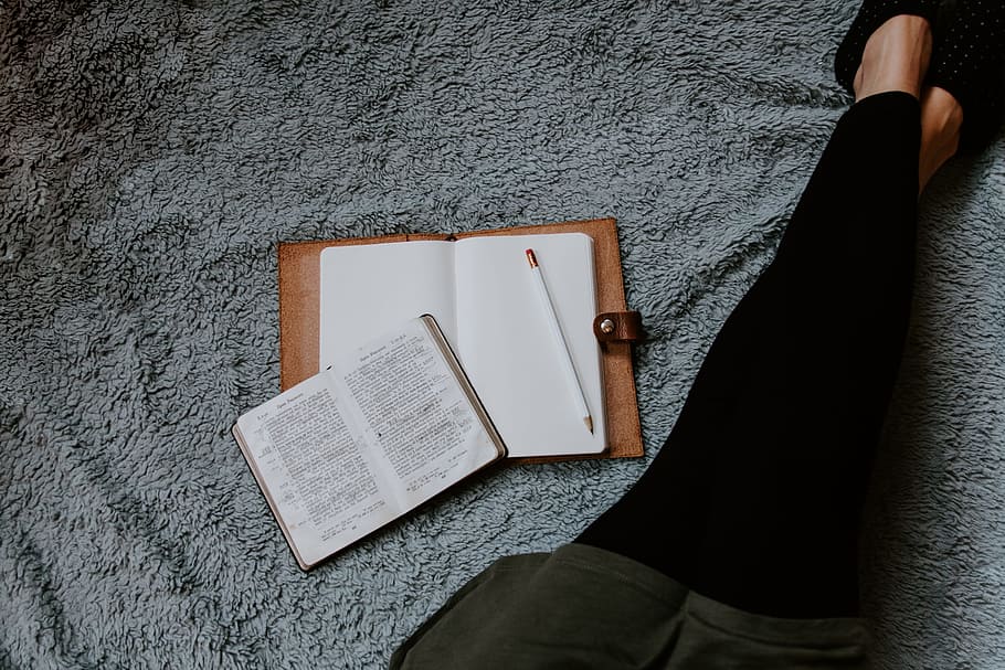 opened white book placed near woman leg on grey surface, pencil HD wallpaper