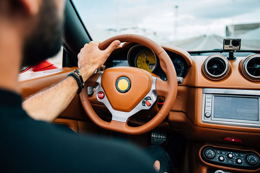 A bearded young man on driving a car with focus on dashboard and steering wheel