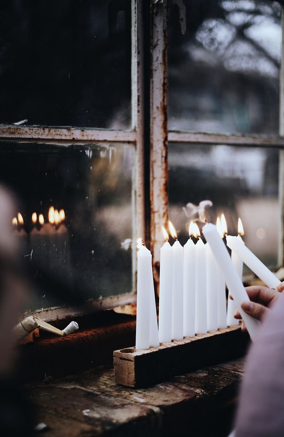 person lighting white candlesticks in a rack near glass windowpane, HD wallpaper