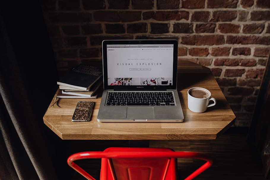 Creatives desk with laptop, camera, journals and books in front of brick wall HD wallpaper