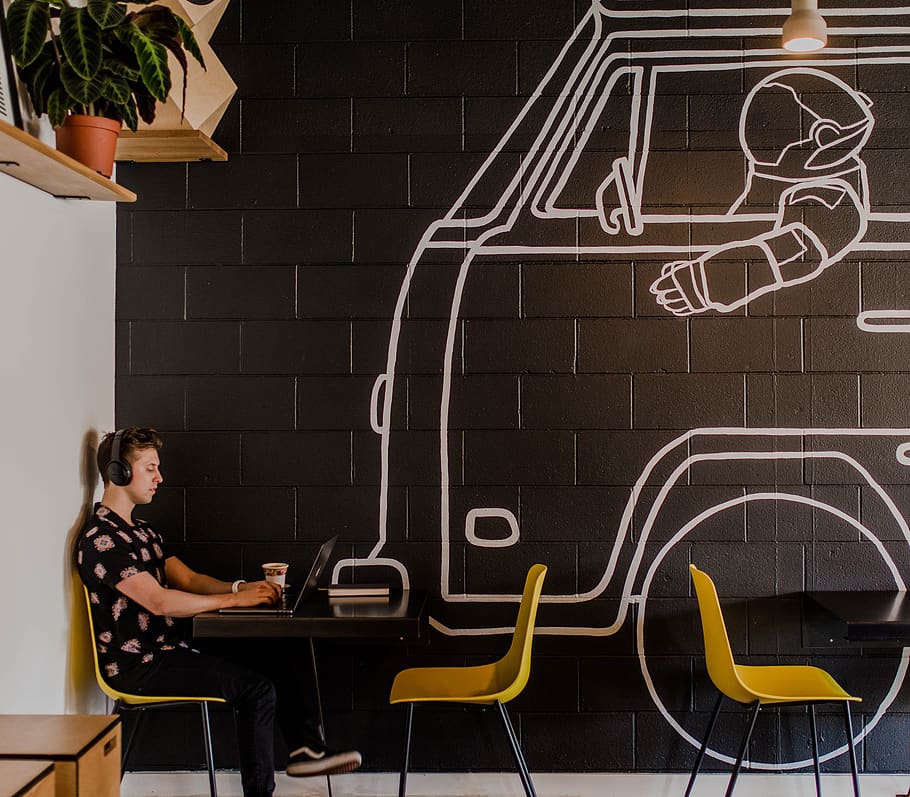 man wearing headphone using laptop while sitting beside table inside cafe HD wallpaper