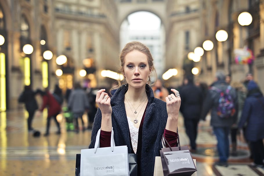 A young blonde woman wearing an overcoat holding shopping bags in her hands