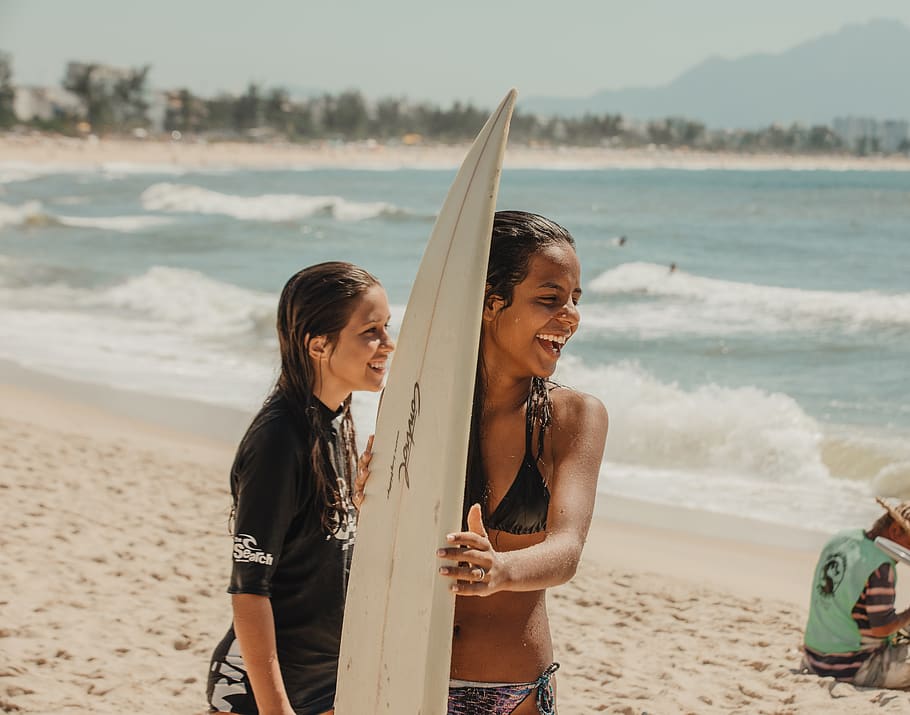 smiling woman holding surfboard while standing on shore, water