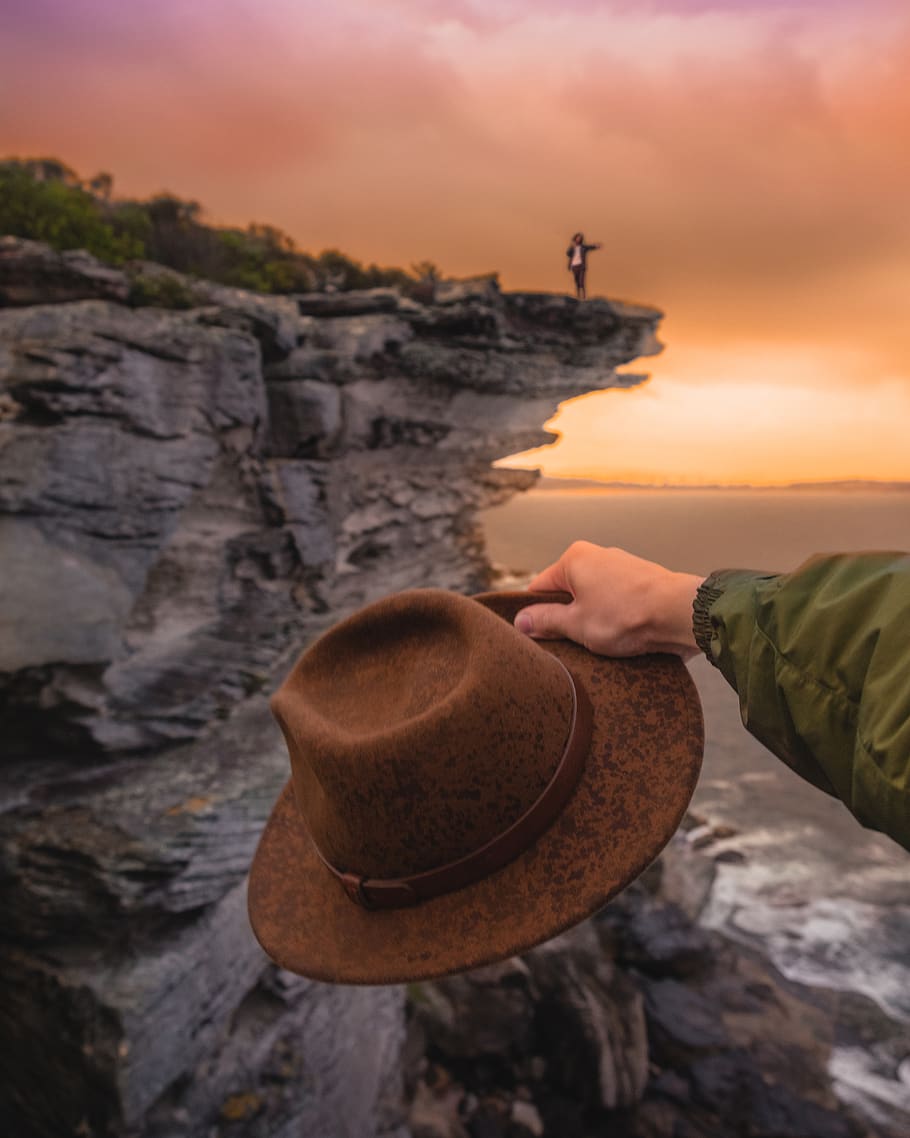 man about to throw his hat at the sea in front of man waving at the edge of the cliff, HD wallpaper