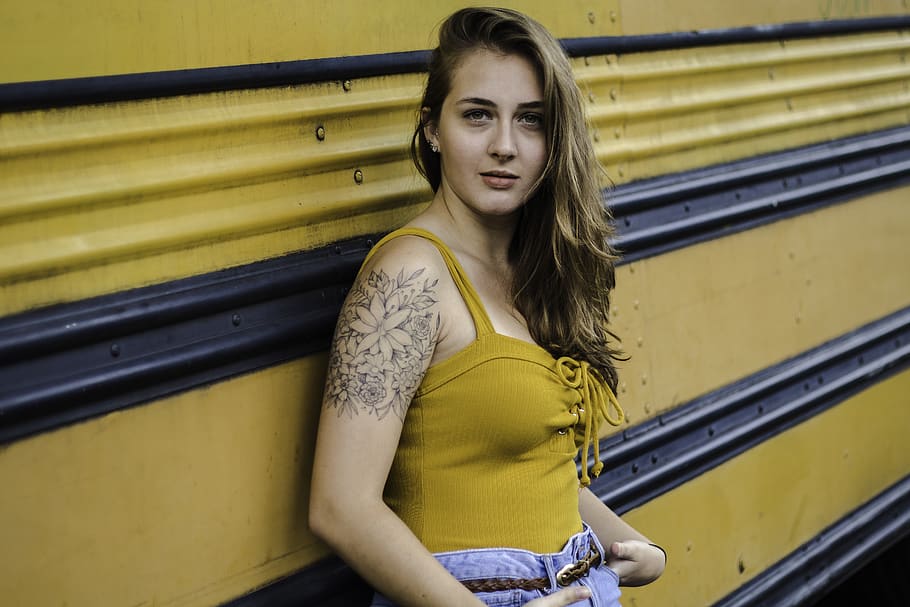 Woman With Arm Tattoo Wearing Yellow Lace-up Tank Top and Blue Denim Bottoms Leaning on Yellow and Black Metal, HD wallpaper