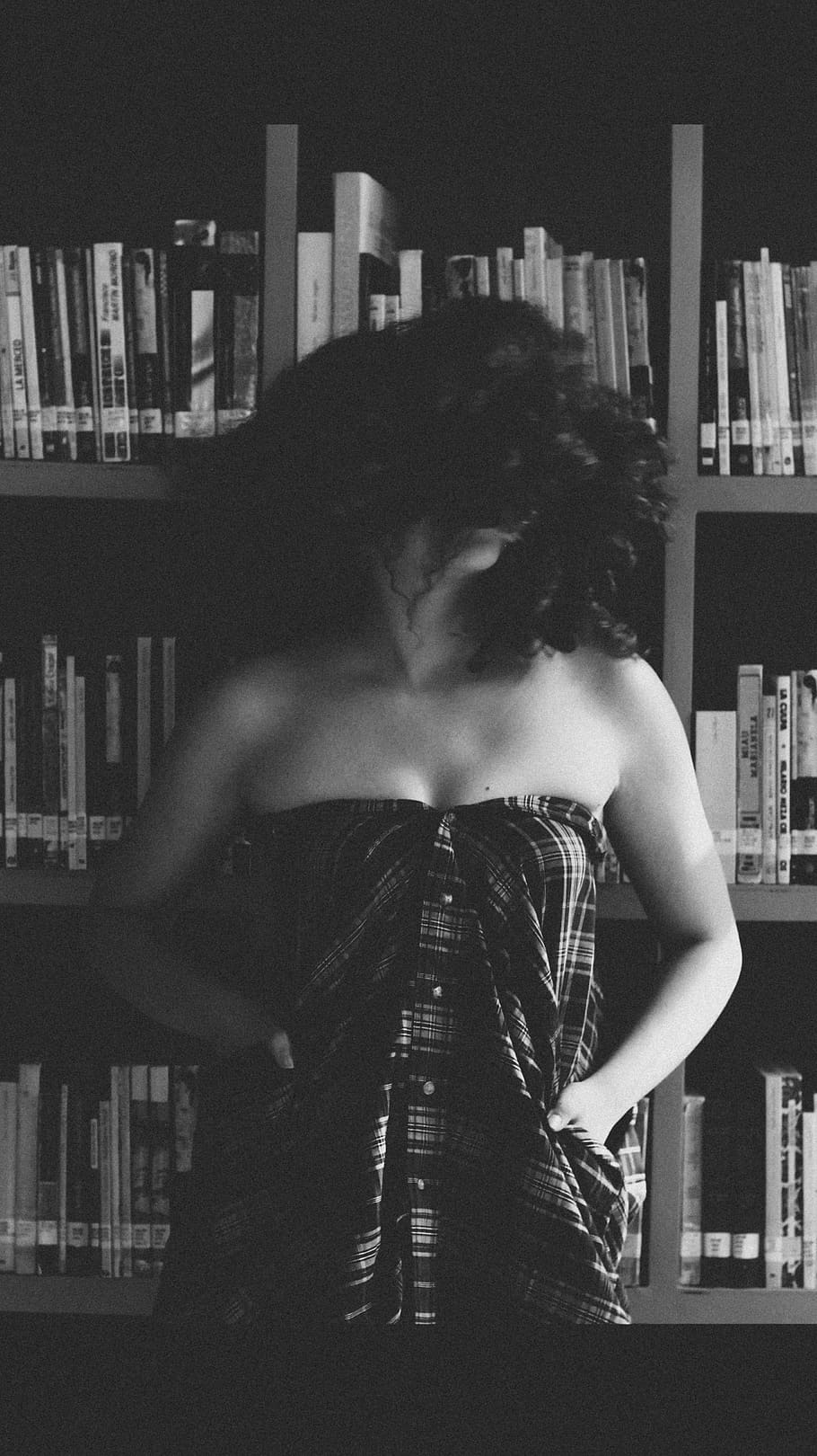 grayscale photography of woman wearing brown bottoms with curly hair standing beside bookshelf, HD wallpaper
