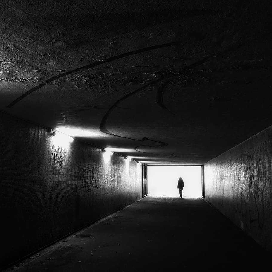 grayscale photography of man standing in tunnel, person, human