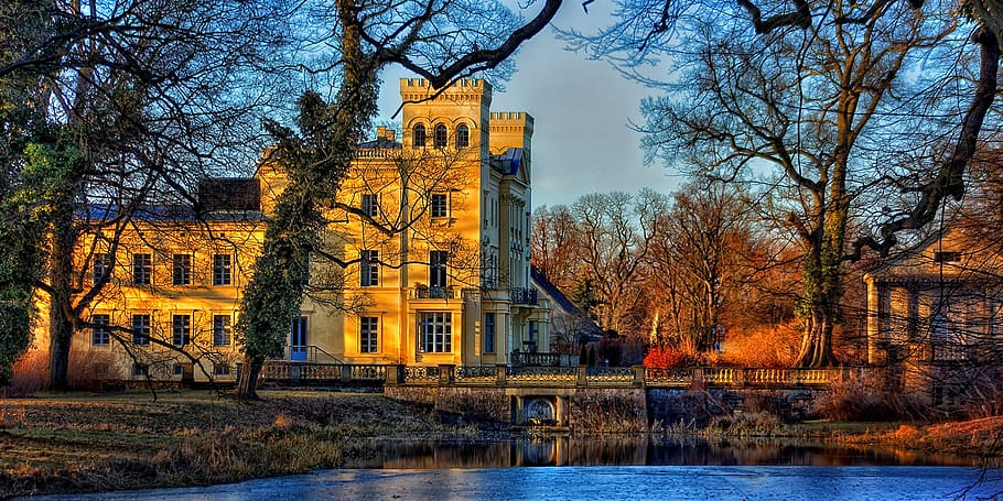 Brown Concrete Building Near Brown Tress Beside Blue Body of Water during Daytime HD wallpaper