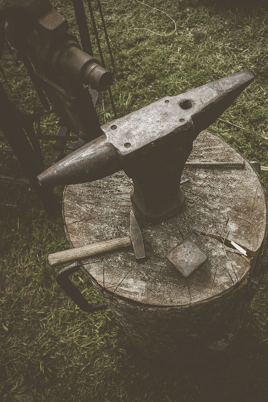 metal anvil on cut log with hammers, no people, grass, old, rusty