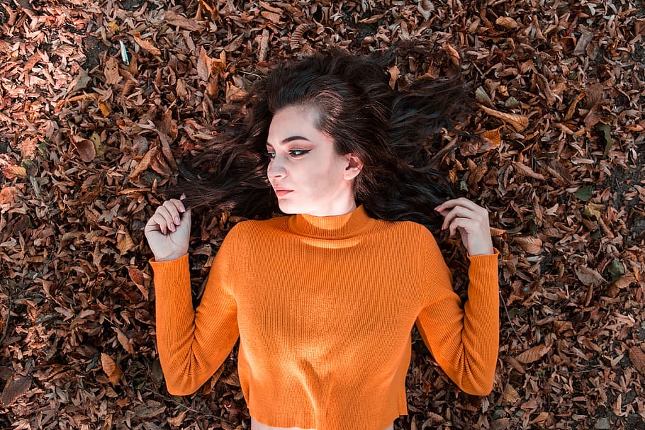 woman wearing orange long-sleeved shirt lying on brown ground with leaves, HD wallpaper