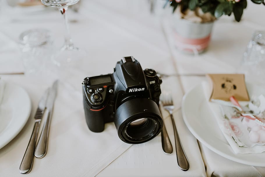 black Nikon camera between plates on table, electronics, tech HD wallpaper