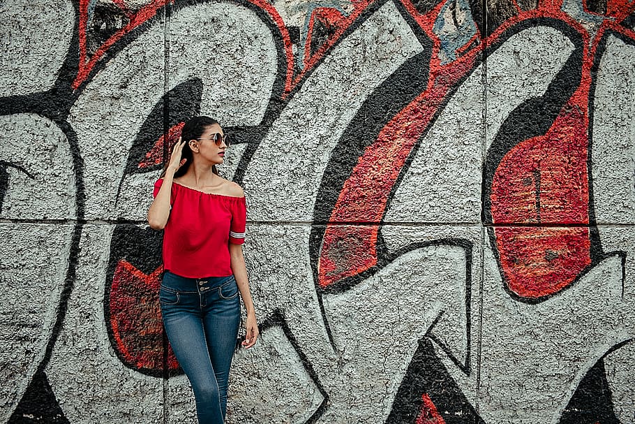 Woman Wearing Red Off-shoulder Shirt and Blue Denim Stone-wash Jeans Near Red and Gray Graffiti Wall