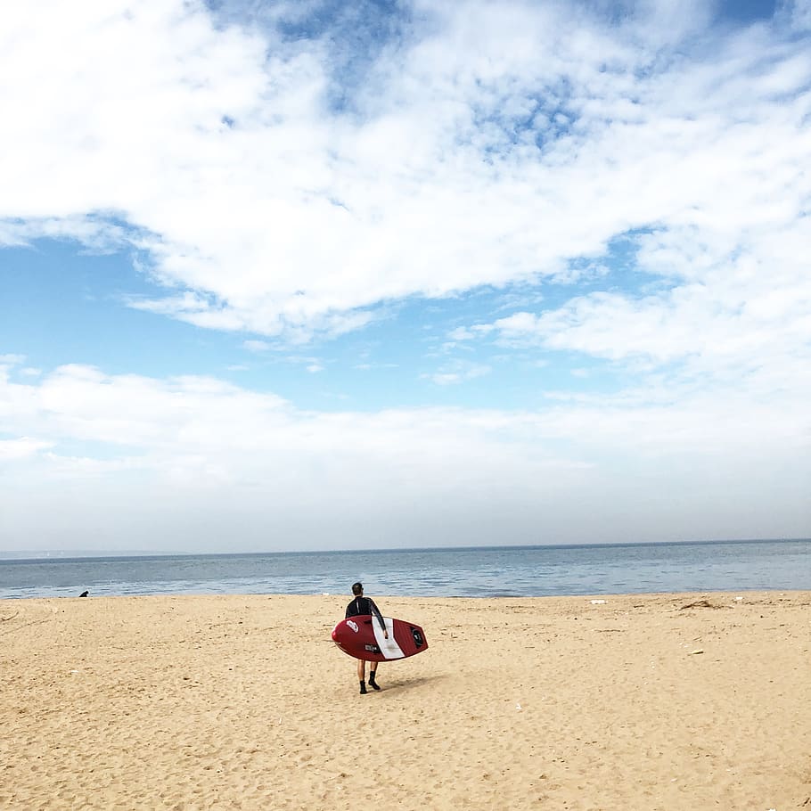 Person Holding Red And White Surfboard Near Sea Under Blue Sky HD wallpaper