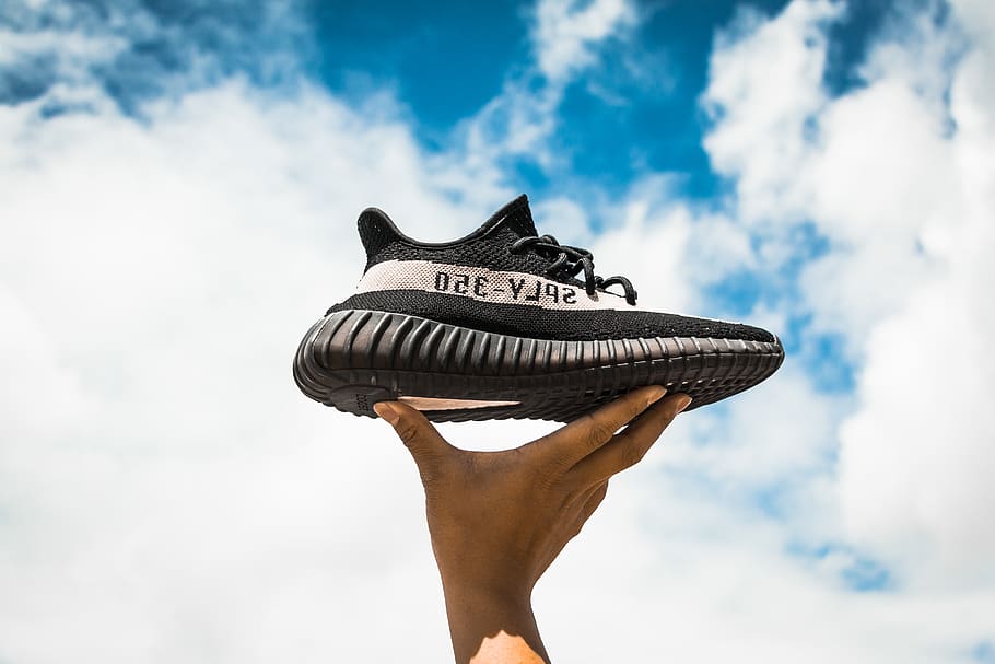 unpaired adidas Yeezy Boost 350 V2 shoe on person's hand, cloud - sky