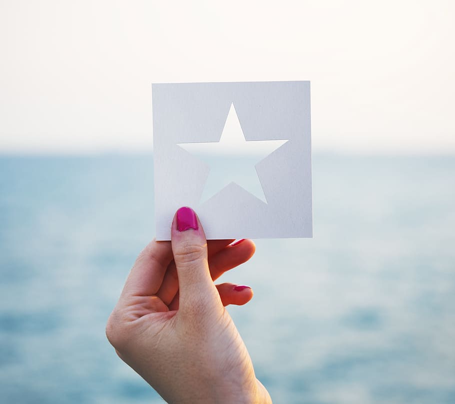 A female hand holding a star shaped paper cut out template with ocean in the background, HD wallpaper