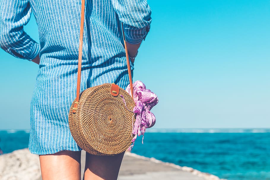 Woman Wearing Blue and White Striped Dress With Brown Rattan Crossbody Bag Near Ocean
