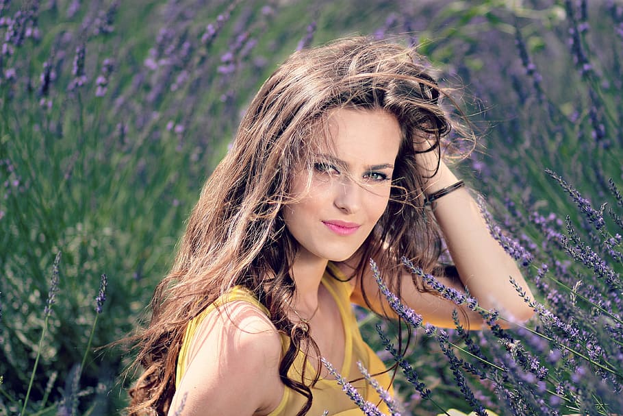 Women's Yellow Tank Top Holding Her Brown Curly Hair While Sitting on a Purple Flower HD wallpaper