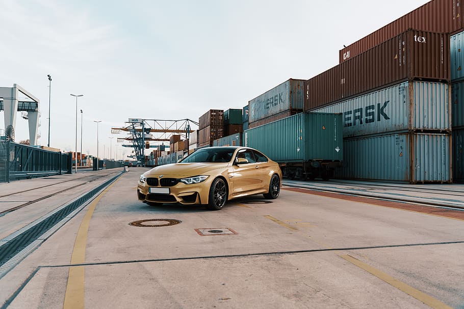 yellow BMW sedan parked near containers during daytime, car, automobile, HD wallpaper