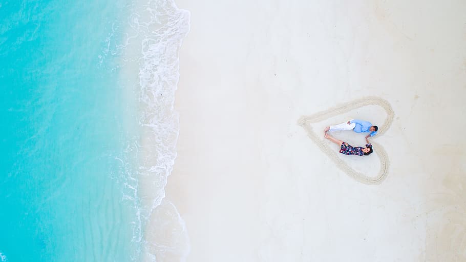 Man and Woman Lying on White Sand Near Sea Shore, aerial view