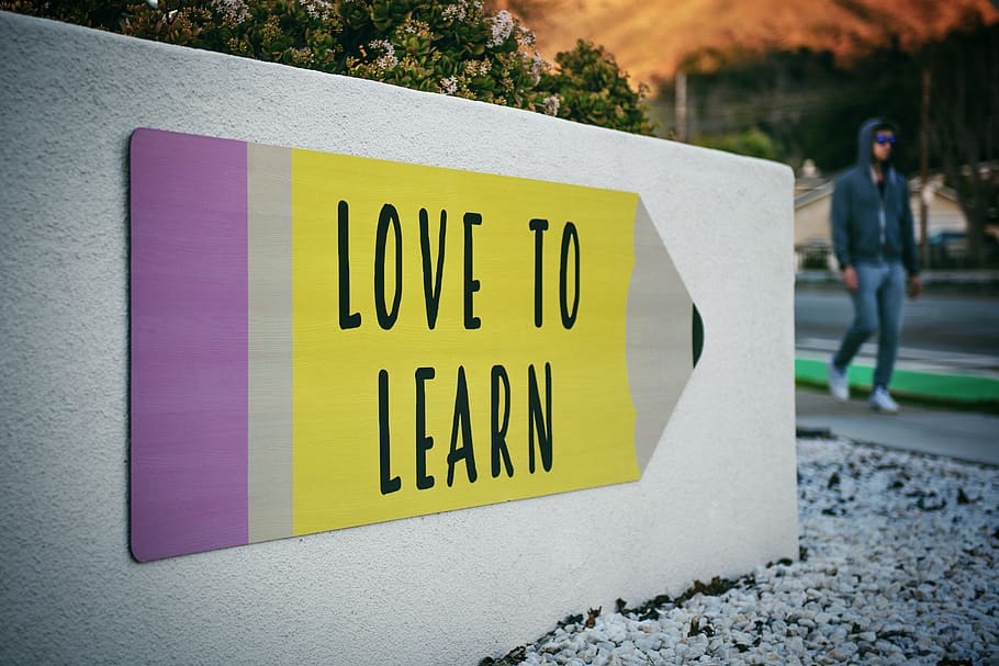 love to learn pencil signage on wall near walking man, text, person