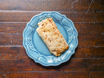 Top view of spinach, feta cheese, and egg all wrapped in a tortilla. Sitting on a blue plate in the sunlight. HD wallpaper
