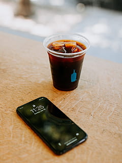 black iPhone 7 beside clear disposable cup filled with beverage with ice cubes HD wallpaper