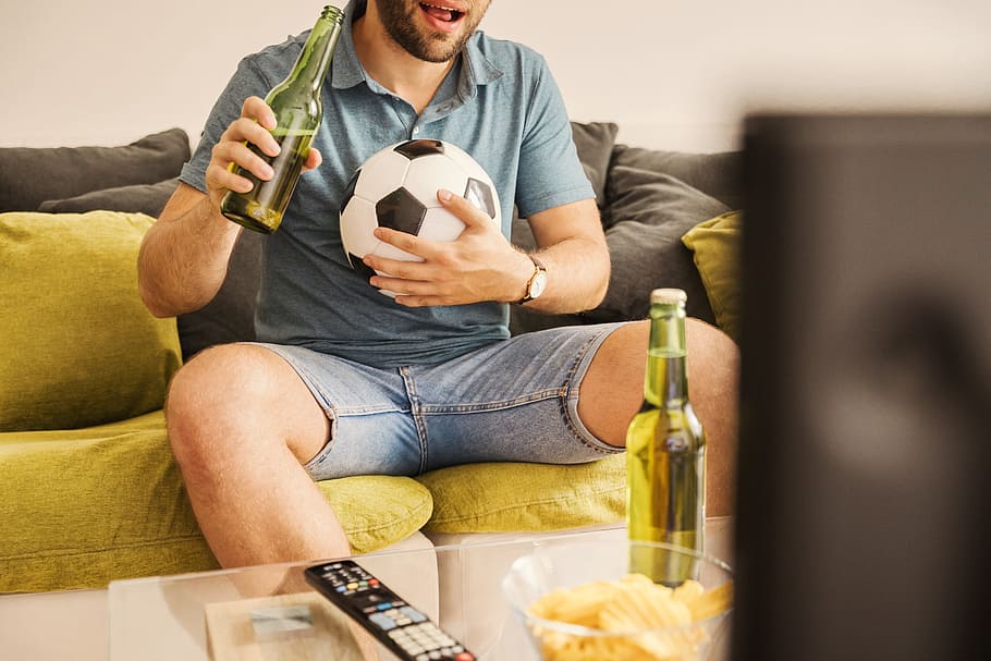 HD wallpaper: Young man watching football on TV and drinking beer at home, ...