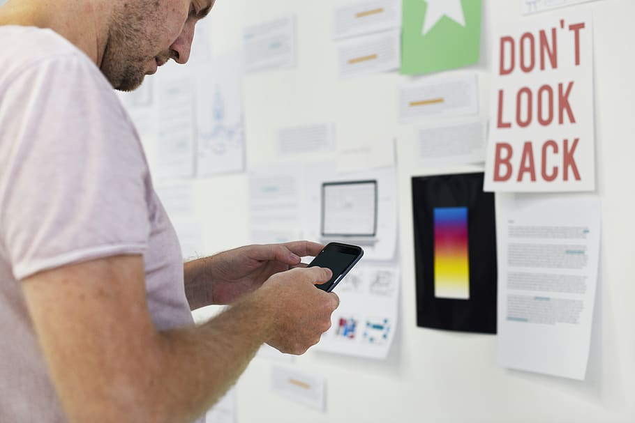 Man Using Smartphone on Front of Wall With Don't Look Back Signage HD wallpaper
