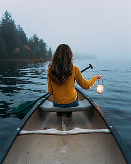 woman sitting and holding lamp on wooden canoe viewing calm body of water HD wallpaper