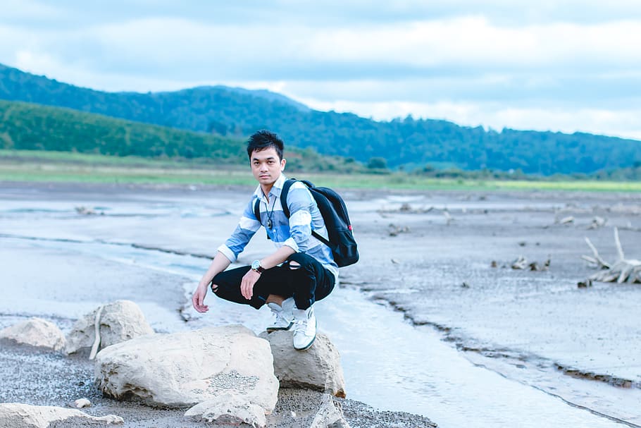 Man on Gray Rock Beside Body of Water, backpack, daylight, landscape HD wallpaper