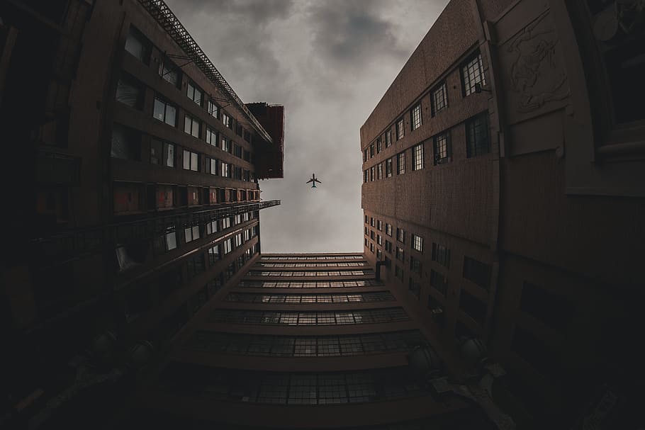 low-angle photo of airliner in flight above high-rise buildings HD wallpaper