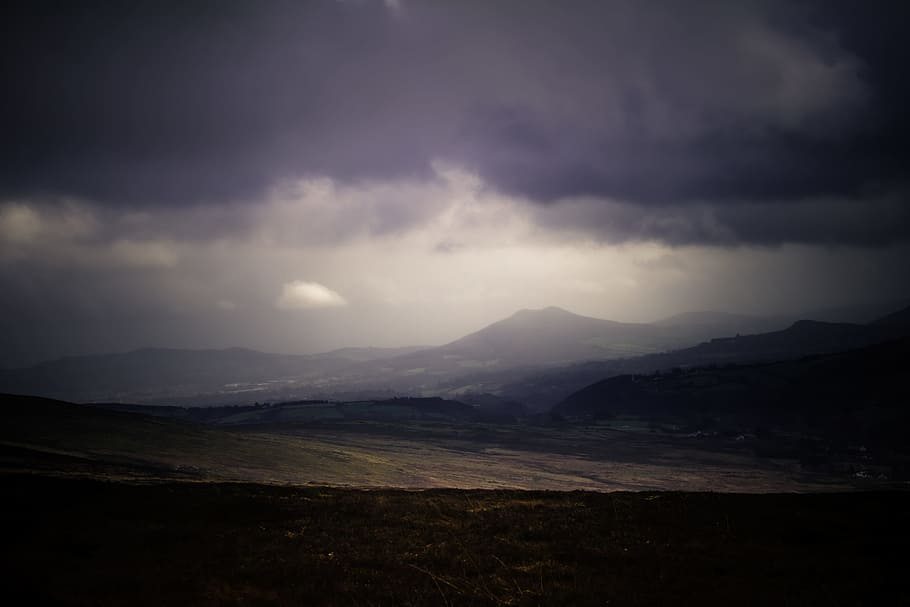 A dim shot of plains stretching to the low mountains on the horizon under gray clouds HD wallpaper