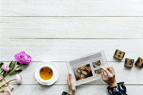 Top View of Person Using Tablet Computer Beside Teacup and Saucer With Brown Tea on Table Top HD wallpaper