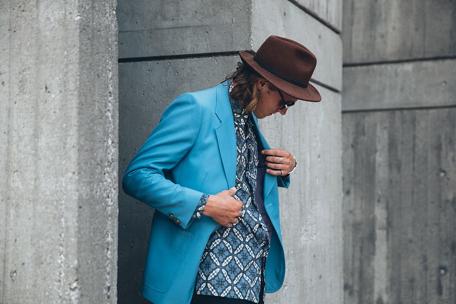 A young caucasian man wearing turquoise blue jacket and brown hat posing outdoors