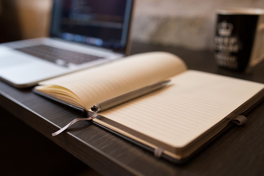 Grey Click Pen on Opened White Lined Book Beside Opened Macbook Pro on Table HD wallpaper
