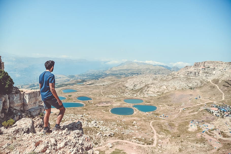 man standing on rocks looking down, cliff, view, lake, trail HD wallpaper