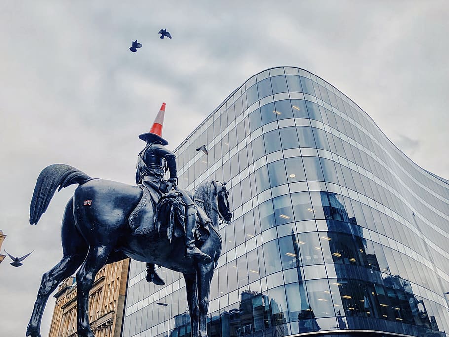 man riding on horse statue near glass high-ride building, office building
