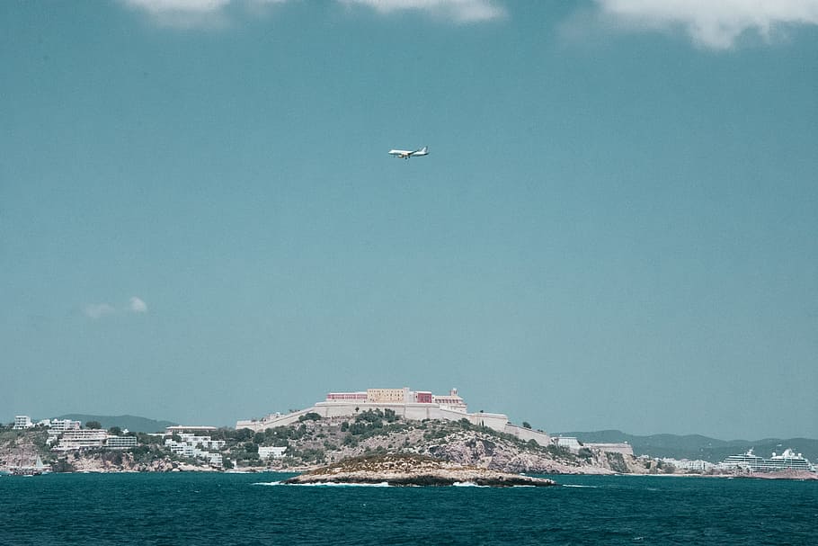 White Airplane Flying over a City Under Blue and White Cloudy Sky HD wallpaper