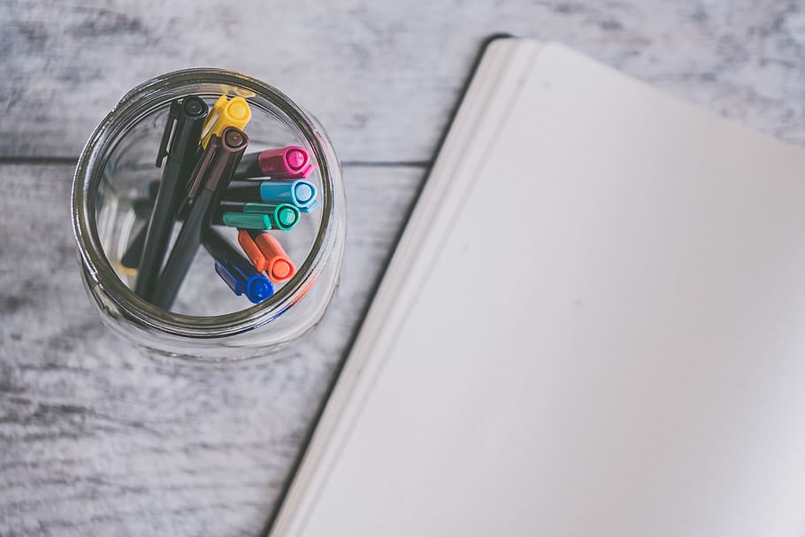 Clear Glass Jar Filled of Coloring Pens Beside of White Sketch Pad HD wallpaper