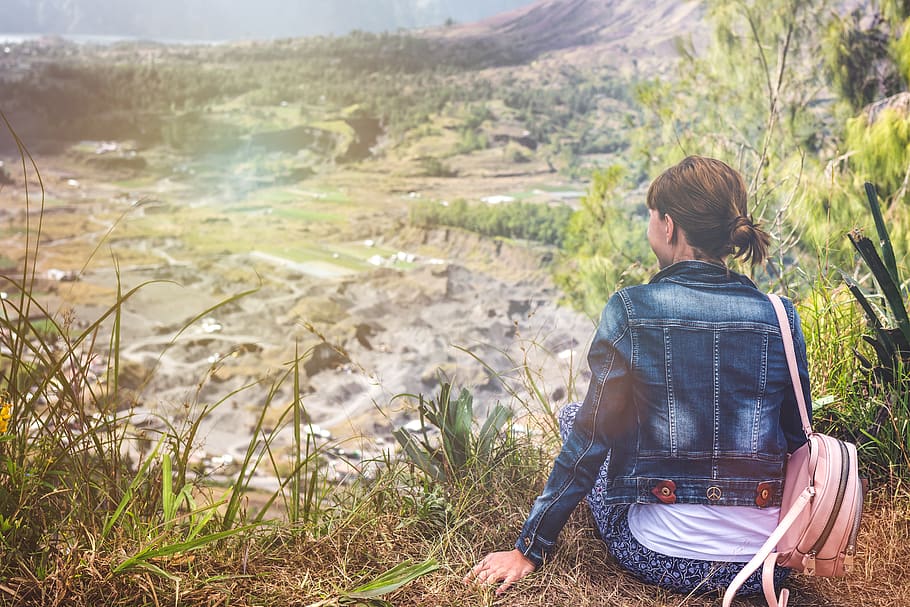 Woman Wearing Blue Denim Jacket Sitting on Cliff Overlooking Open Field HD wallpaper